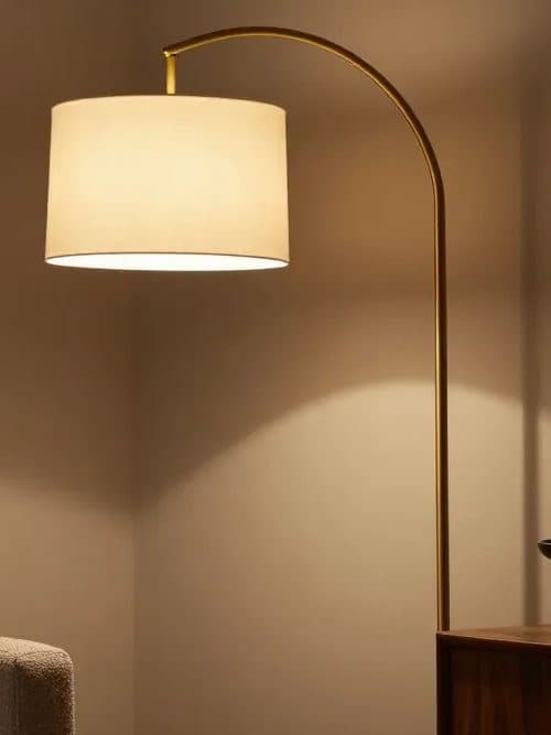 Arched brass floor lamp with a linen drum shade, glowing in a quiet corner