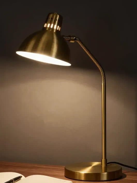 Brushed brass desk lamp with a dome shade, lit